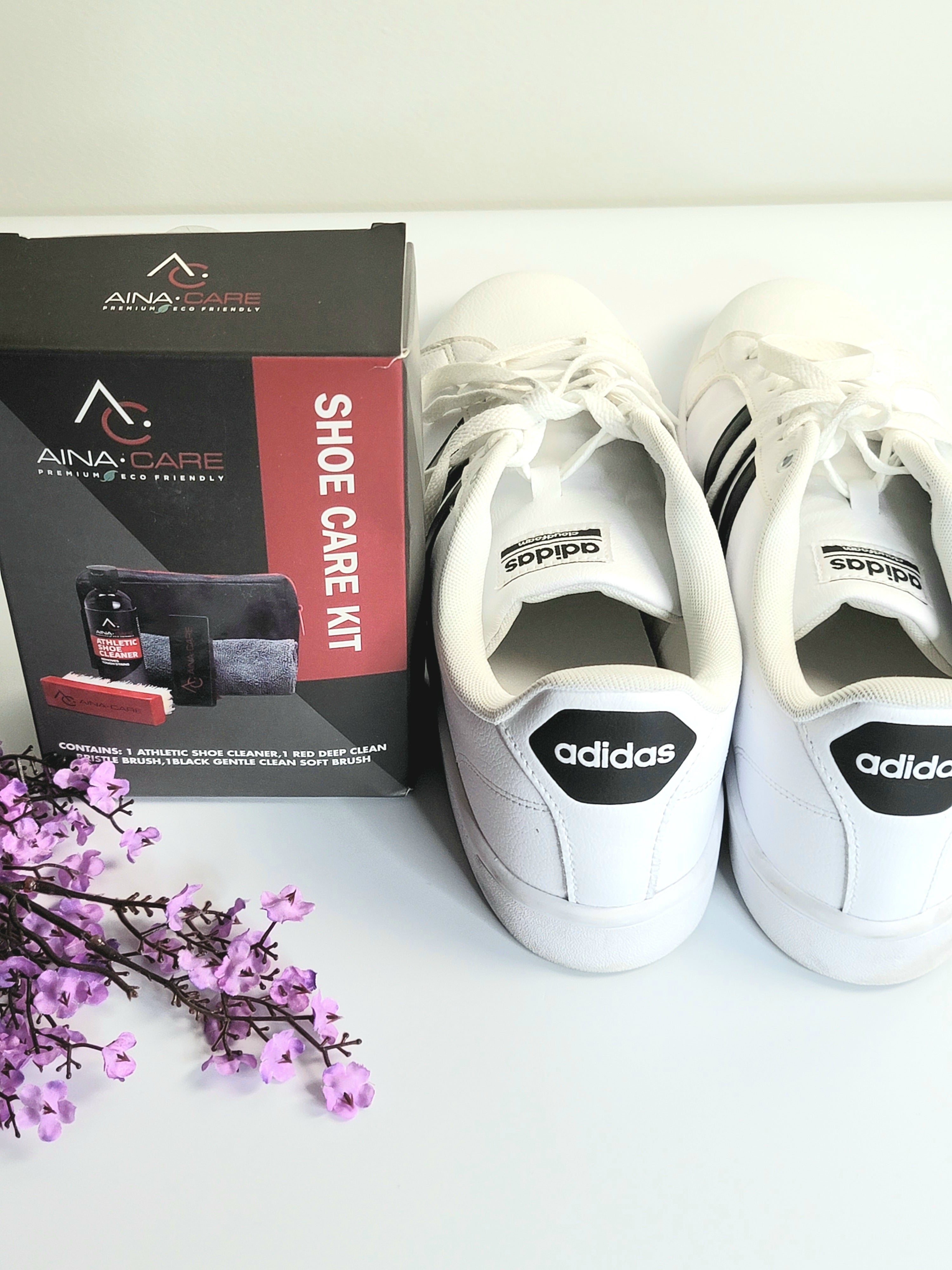 Silver Shoe Care Kit still in it's box next to a pair of clean, white Adidas sneakers and flowers on a white table.