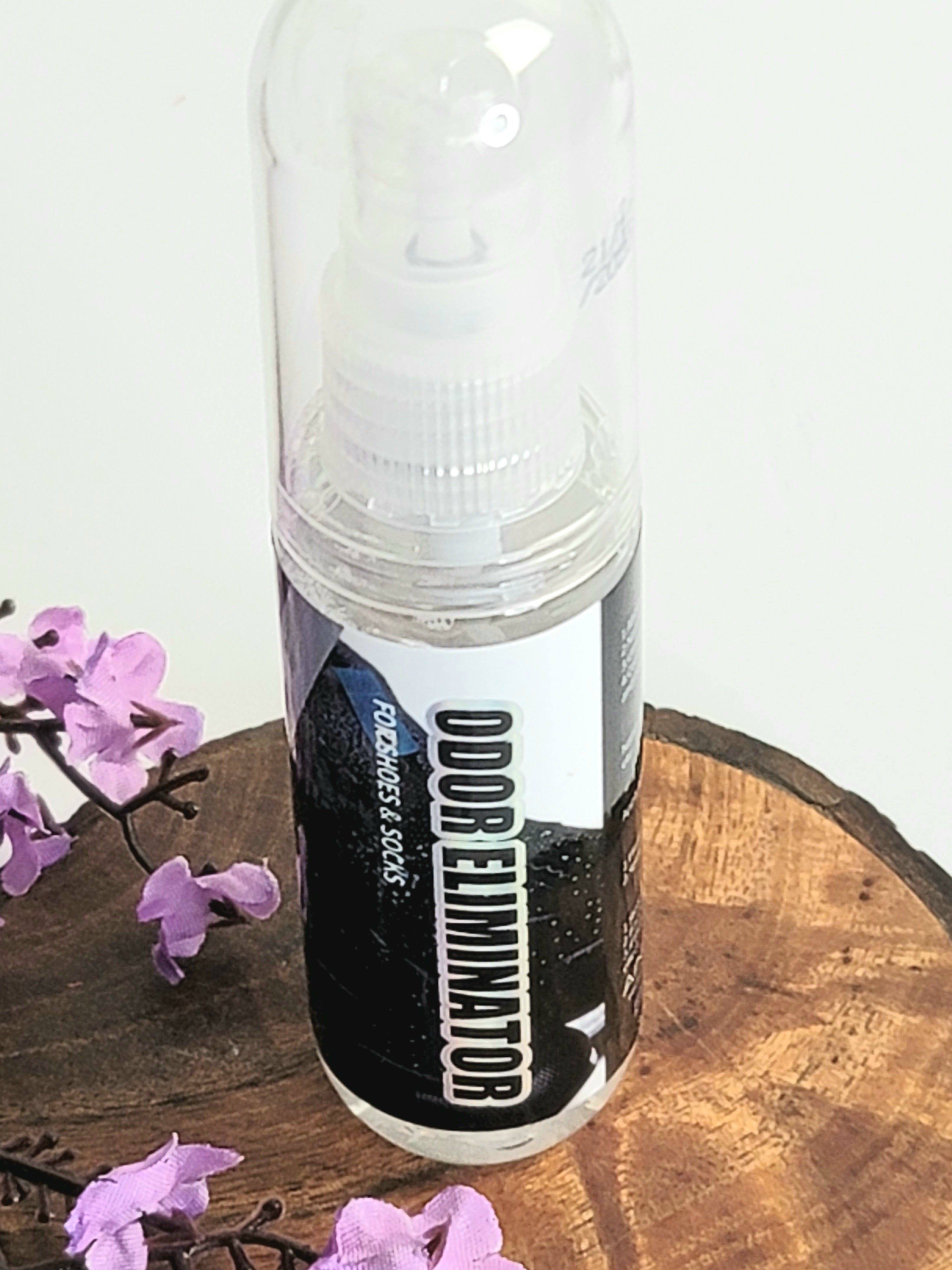 Close up on a bottle of Odor Eliminator from AinaCare sitting on a wooden stump with purple flowers in the bottom left corner.