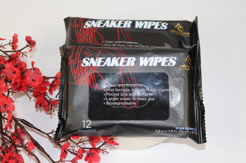 Two packs of All-Purpose Sneaker Wipes from AinaCare sitting next to red flowers on a white background.
