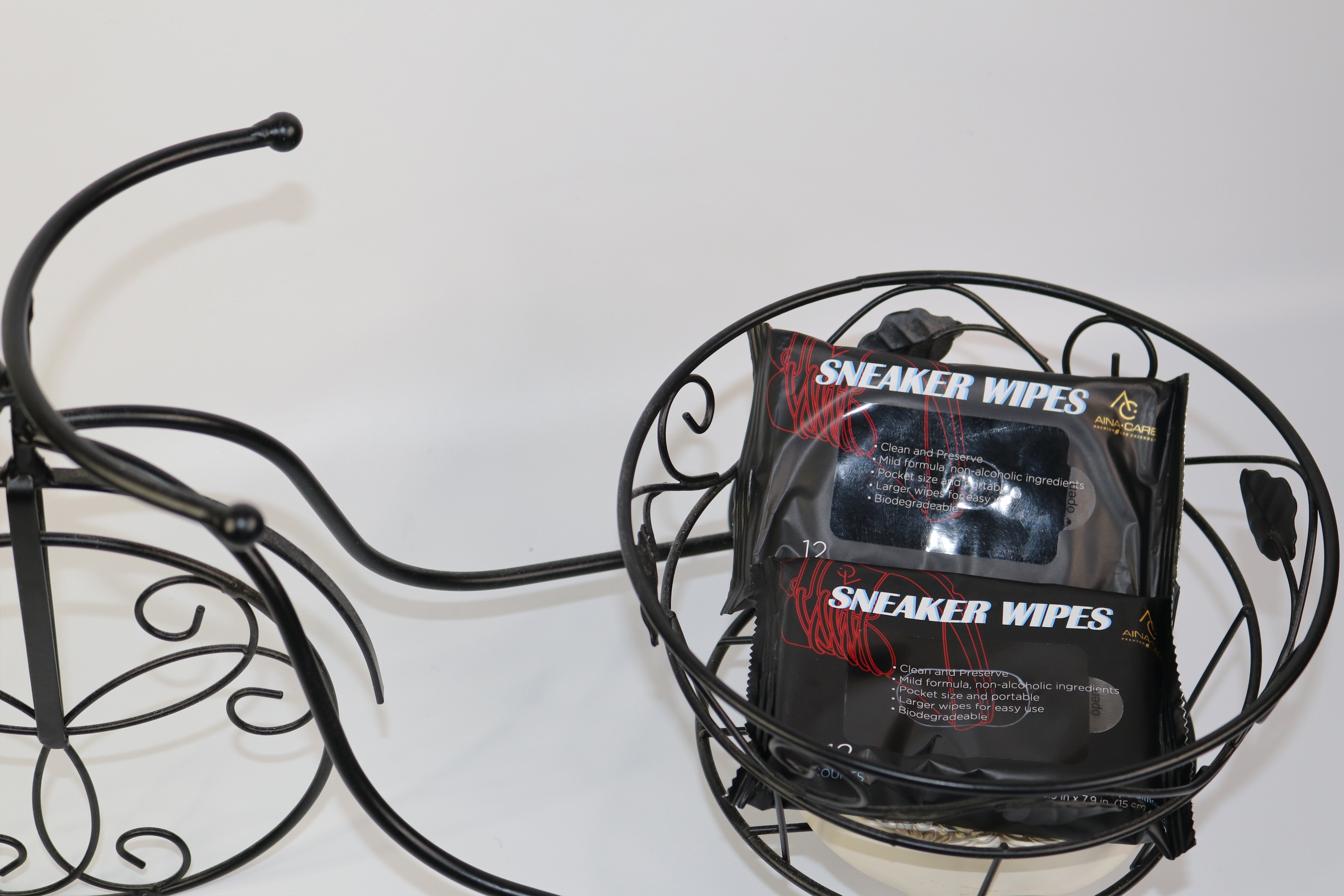 Two packs of All-Purpose Sneaker Wipes from AinaCare inside of a wire bicycle basket on a white background.