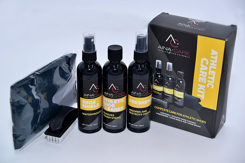 Each item in the Athletic Care Kit from AinaCare is displayed next to the box. Items include a black microfiber cloth, a soft brush, Shoe Shield waterproofer, Athletic Shoe Cleaner solution, and Freshener spray.