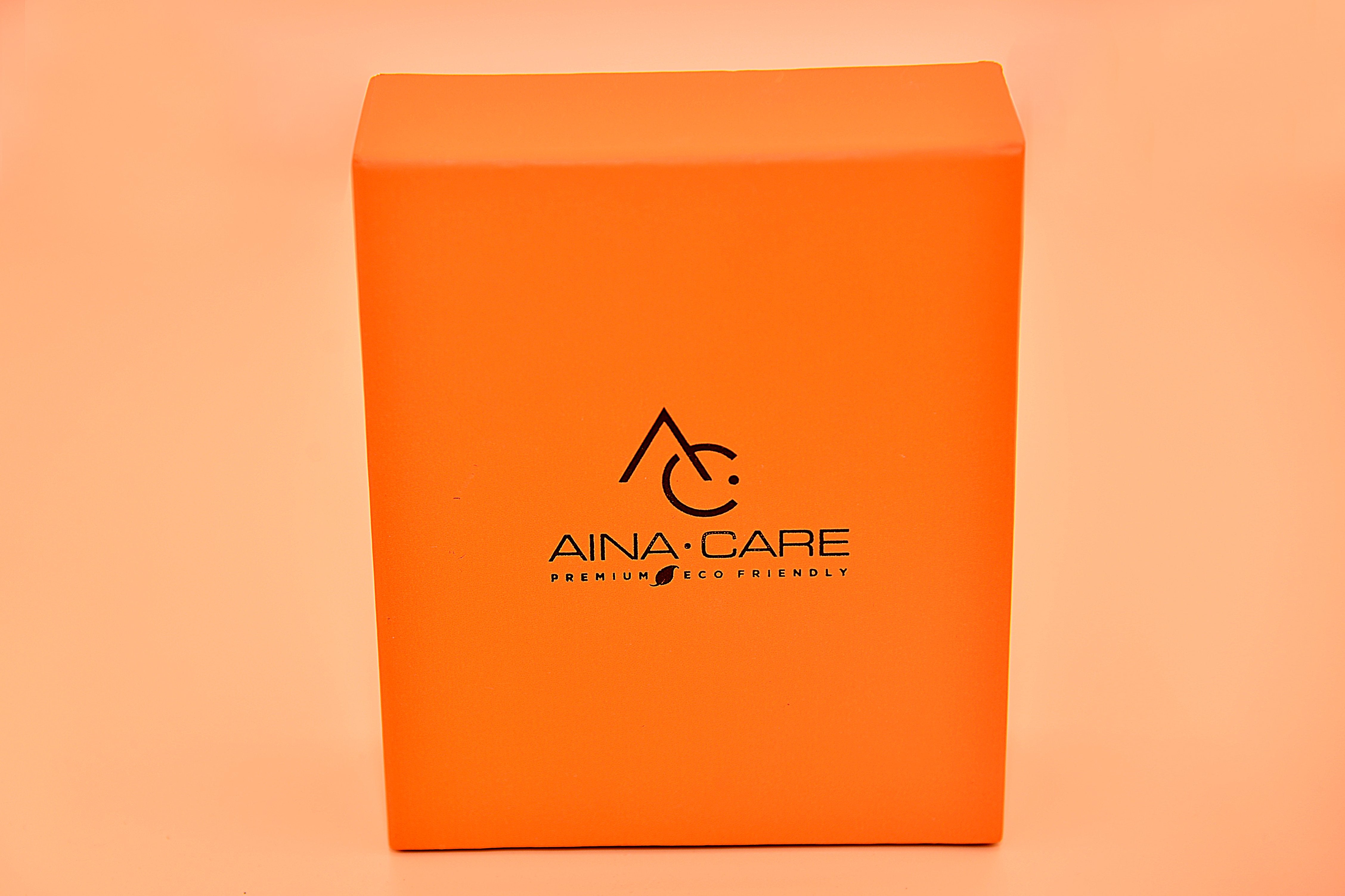Orange, unopened Premium I Shoe Polish Kit from AinaCare on a peach colored backgorund.