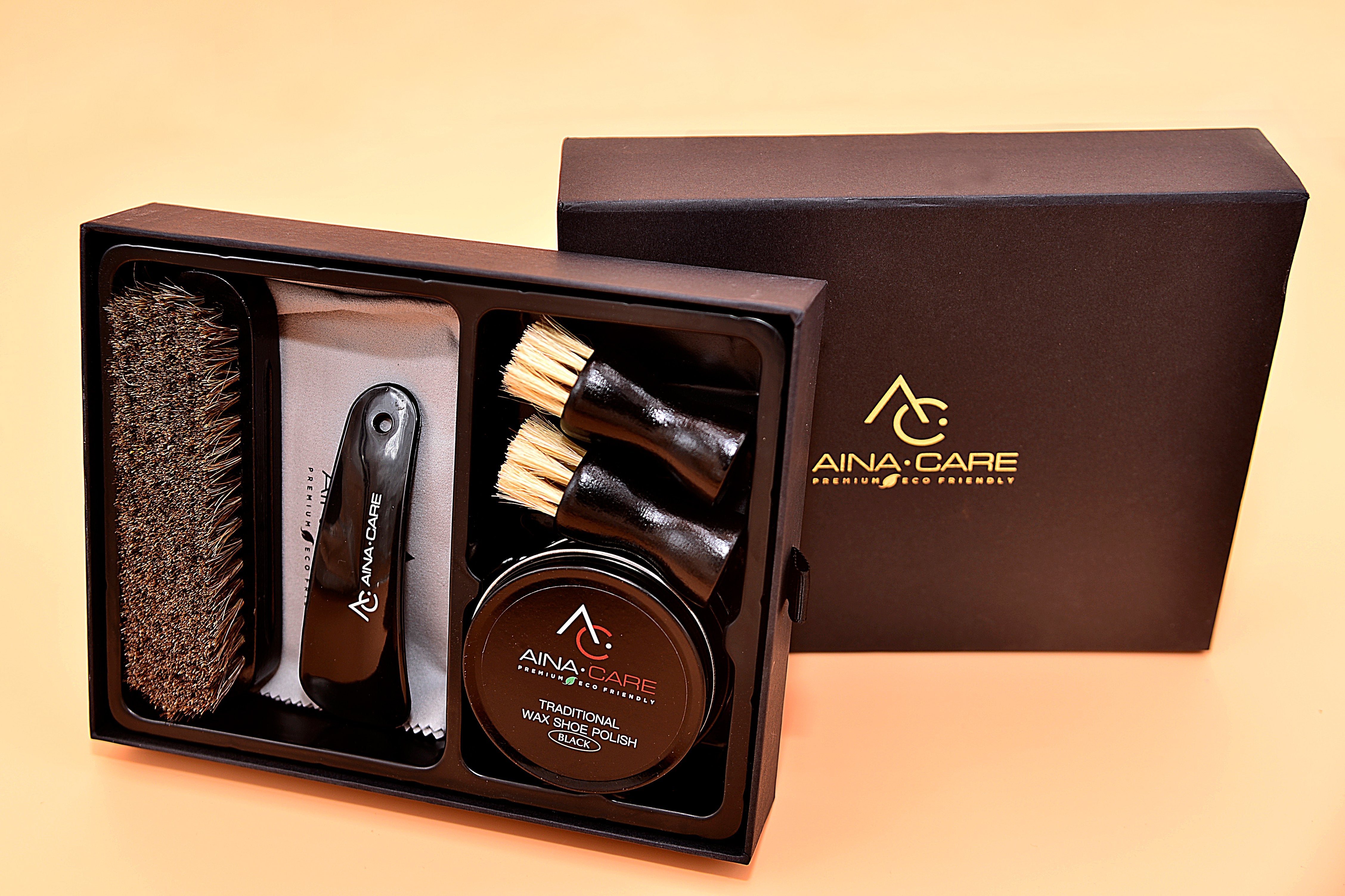 Opened box showing all items included in the Premium II Shoe Polish Kit from AinaCare. Items include a hard brush, two soft brushes, a microfiber cloth, a tub of wax polish.