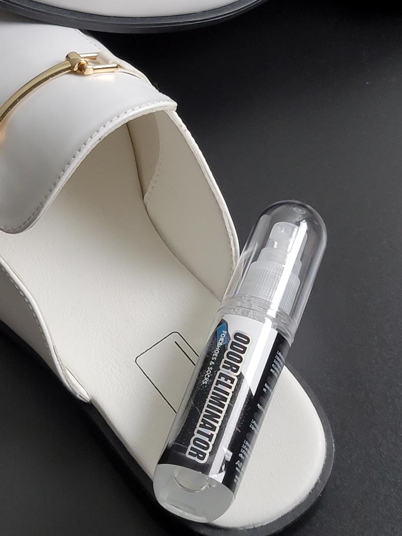 A bottle of Odor Eliminator from AinaCare sitting in a white leather loafer shoe.